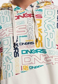 Hooded sweatshirt featuring a cream base with multicolored "DNGRS" text in various sizes and orientations. Textured drawstrings with metal tips.