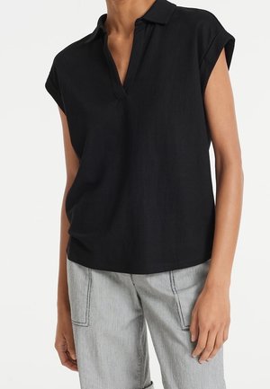 Czarna koszula z krótkim rękawem i kołnierzykiem, wykonana z lekkiego materiału, o luźnym kroju i subtelnej fakturze. Do tego szare spodnie w paski.