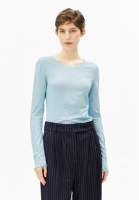 Hellblaues langärmeliges Oberteil mit rundem Ausschnitt, kombiniert mit dunkelblauen, fein gestreiften Hosen. Der Stoff wirkt weich und leicht tailliert.