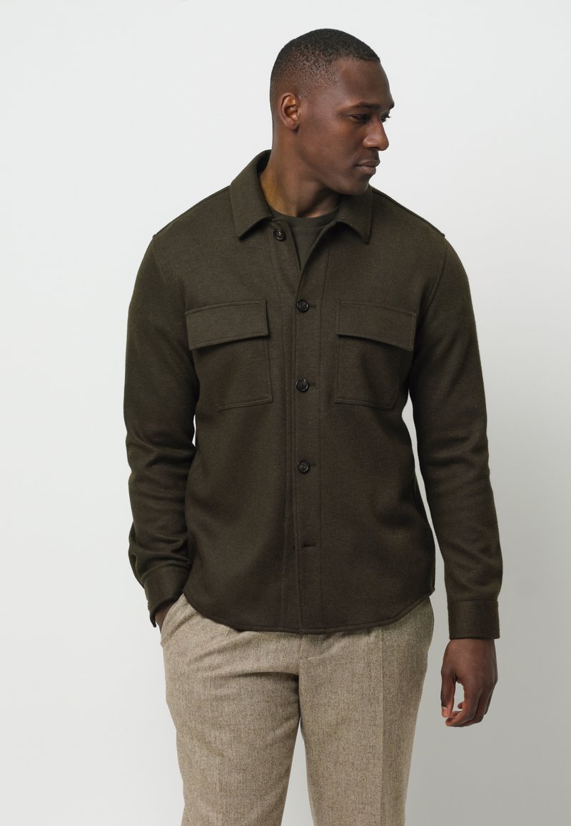 Camicia a maniche lunghe colore verde oliva scuro, realizzata in tessuto testurizzato, con due tasche sul petto e un colletto.