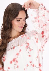 Hvid bluse med pink blomsterprint, off-shoulder design, smocket liv og flæseærmer. Let tekstur i stoffet.