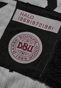 Sort og gråt stof med et cirkulært broderet mærke med "DBU" i maroon og et label med "HALO 196819721981" i rødt.