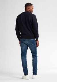 Felpa blu navy in tessuto testurizzato, con scollatura a girocollo e polsini a costine. Indossata con jeans blu e sneakers bianche, vista da dietro.