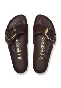 Een paar donkerbruine Birkenstock slide-sandalen met grote gouden gespen en maatmarkeringen op de voetbed, van bovenaf weergegeven.