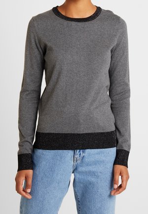 Personne portant un pull gris à manches longues avec col, poignets et ourlet côtelés noirs, assorti à un jean bleu clair, debout face à l’avant.