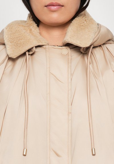 Doudoune beige avec un col en peluche beige, cordons de serrage avec des accents dorés et texture douce. Présente un design plissé et une fermeture à boutons.