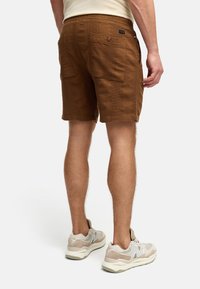 Brune teksturerede shorts med en tætsiddende design, der har to baglommer og subtile syninger. Kombinationen med lyse beige sneakers.