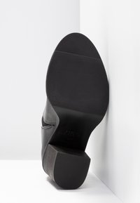 Botín negro hasta el tobillo con un exterior sintético texturizado, tacón bajo en bloque y suela de goma con ranuras horizontales para mayor tracción.