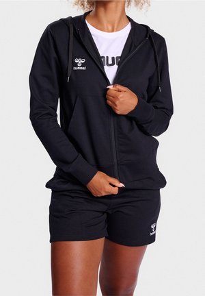 Sweat à capuche noir zippé avec une poche frontale, en tissu texturé, associé à un short noir avec un logo. Vêtements de sport décontractés et élégants.