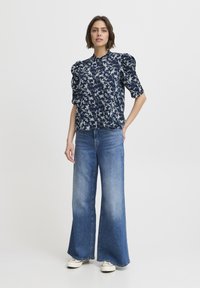 Navy floral-patterned blouse with puff sleeves, paired with wide-leg light blue jeans and white sneakers. Simple collar design, casual fit.