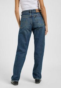 Blaue Jeans aus Denim mit einem lockeren Schnitt, hinteren Taschen und einem braunen Leder-Logo-Patch am Bund. Klassisches Fünf-Taschen-Design.