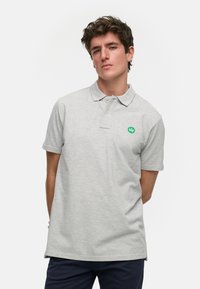 Grå polo-shirt laget av bomull, med en grønn logo på venstre bryst, korte ermer og en klassisk kragedesign.