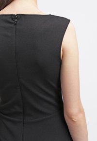 Svart ärmlös klänning med en åtsittande design, slät textur och en subtil dragkedjedetalj på baksidan. Inga synliga mönster eller detaljer.