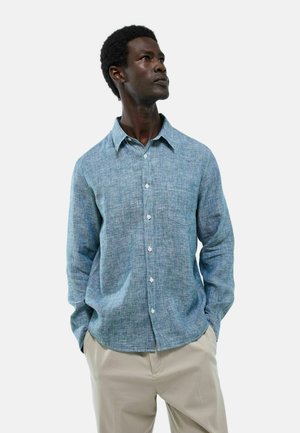 Chemise bleu clair à manches longues en tissu texturé, dotée d'un devant à boutons, d'un col pointu et d'une poche poitrine unique.