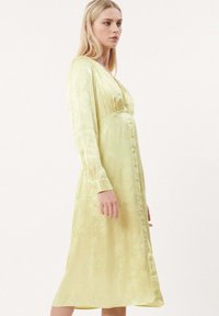 Hellgrünes, langärmliges Kleid mit V-Ausschnitt, geraffter Taille und einer Reihe von Knöpfen auf der Vorderseite. Glatte, seidige Textur mit dezentem Glanz.