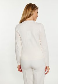 Hellbeige, gerippter Pullover mit langen Ärmeln, figurbetontem Design und Rundhalsausschnitt, kombiniert mit hellen Hosen, von hinten gezeigt.