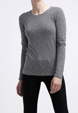 Osoba ubrana w dopasowaną, długorękawową koszulkę w poziome szaro-czarne paski oraz czarne spodnie na jednolitym białym tle.