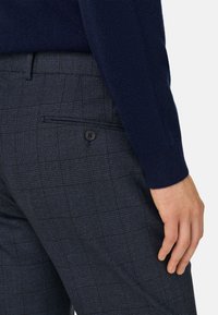 Mörkblå stickad tröja i kombination med blå rutig ullbyxa som har en bakficka och knapppresentation. Båda plaggen har en strukturerad tygdesign.