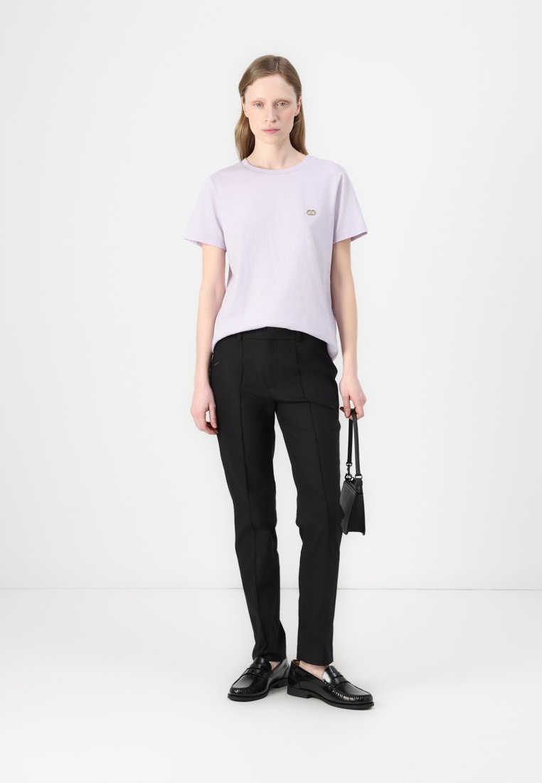 T-shirt violet clair à manches courtes avec un petit logo, associé à un pantalon noir ajusté et des chaussures noires. Design simple, accents minimalistes.