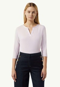 Hellblaues, langärmliges Oberteil mit V-Ausschnitt, kombiniert mit dunkelblauen Jeans mit goldenen Knopfdetails an der Seite.