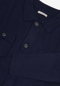 Camisa de punto color azul marino con botones y cuello, que presenta dos bolsillos frontales y botones negros. Textura suave con detalles acanalados.