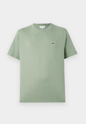 Camiseta de algodón verde claro con cuello redondo, mangas cortas y un pequeño logo en el lado izquierdo del pecho. Textura suave, ajuste estándar.