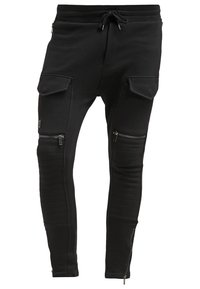 Svarta joggerbyxor gjorda av mjukt material, med dragkedjefickor, ruggad detalj vid knäna och dragsko i midjan.