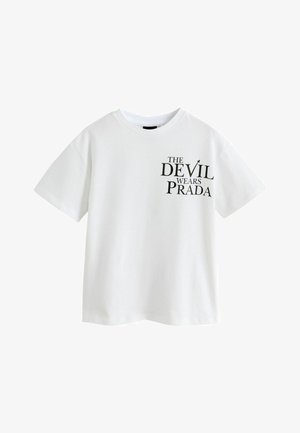 Hvid T-shirt med korte ærmer og sort tekst på venstre bryst, der siger "The Devil Wears Prada" i forskellige skriftstørrelser.