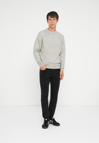 Gray knitted sweater with a crew neck, set against black jeans and black sneakers, in a minimalist studio background.