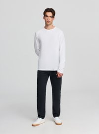 Biały bawełniany T-shirt z długim rękawem, okrągły dekolt, zestawiony z czarnymi jeansami i białymi trampkami z beżową podeszwą. Prosty wzór z minimalną ilością detali.