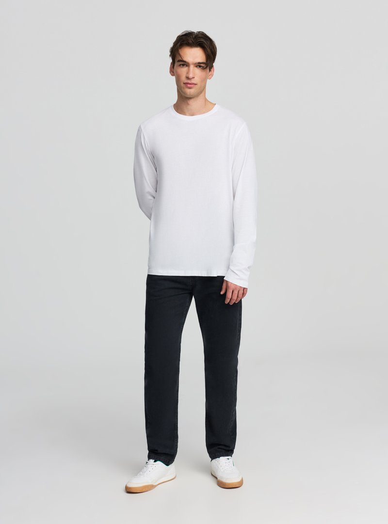 Biały bawełniany T-shirt z długim rękawem, okrągły dekolt, zestawiony z czarnymi jeansami i białymi trampkami z beżową podeszwą. Prosty wzór z minimalną ilością detali.