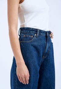 Hochtaillierte, dunkelblaue Jeans aus Denim mit lockerer Passform, kontrastierenden Nähten, fünf Taschen und einem Bund mit Gürtelansatz.