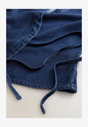 Jeansowa tkanina w głębokim granatowym kolorze, z zaokrąglonymi krawędziami i sznurkami. Tekstura jest gładka z widocznymi detalami przeszyć wzdłuż szwów.