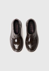 Scarpe slip-on marrone scuro con finitura lucida, punta arrotondata e dettagli elastici laterali. Le solette testurizzate presentano il nome del marchio in un colore a contrasto.