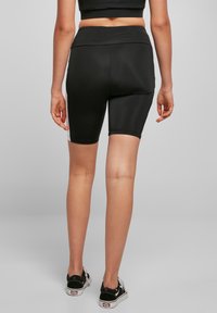 Musta urheilushortsit, jotka istuvat tiukasti, valmistettu sileästä, joustavasta kankaasta, joissa on korkeavyötärö ja vähäiset sauma-yksityiskohdat.