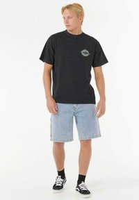 Sort kortærmet t-shirt med farverig grafik på brystet, parret med lyse denim shorts og sorte sokker med hvide sneakers.