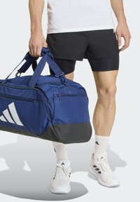 Borsa da viaggio blu con fondo nero, dotata di due manici e cerniere, contrassegnata da un grande logo Adidas bianco e un motivo a punti.