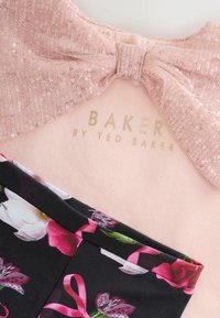 Rožinė palaidinė su blizgučiais surišta kaspinu ir auksiniu užrašu "BAKER BY TED BAKER"; turi juodą gėlių raštuotą sijoną su rožiniais akcentais.