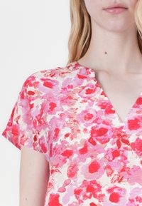 Top a maniche corte con motivo floreale, dotato di scollatura a V, con una miscela di tonalità di rosa e rosso su uno sfondo chiaro, realizzato in tessuto leggero.