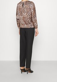 Blusa de estampado de leopardo con un corte holgado y puños elásticos, combinada con pantalones negros de corte suelto y mules negros con tacón.