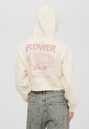 Felpa corta di colore crema con cappuccio. Grafica floreale rosa e testo "Negozio di FIORI" stampato sul retro. Tessuto morbido, vestibilità rilassata.