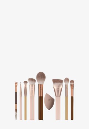 Åtte sminkekoster og en sminkesvamp, ordnet i en rad på hvit bakgrunn, med forskjellige håndtakfarger og børsteformer.