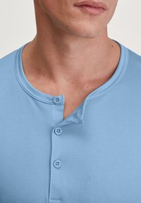 Lichtblauw, shirt met korte mouwen en een ronde halslijn, voorzien van een knoopsluiting met drie knopen en een zachte, gladde stof.