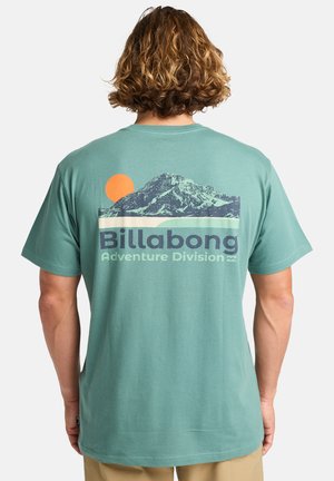 Mintgroene katoenen t-shirt met een graphic van een berg, een oranje zon en de tekst "Billabong Adventure Division" in marineblauw. Korte mouwen.