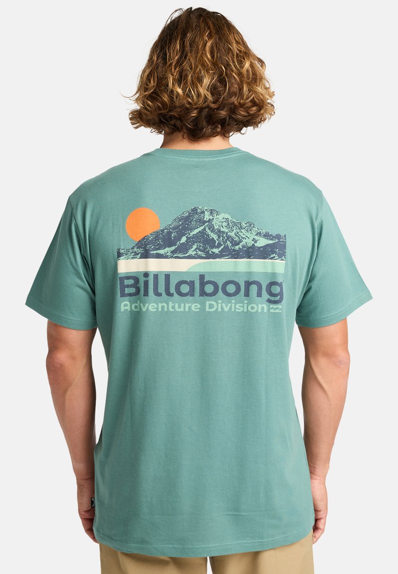Mintgrøn bomuld t-shirt med en grafik af et bjerg, en orange sol og teksten "Billabong Adventure Division" i marineblå. Korte ærmer.