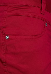 Pantaloni in cotone rosso con un mix di materiali, dotati di una tasca frontale con hardware in argento, dettagli di cucitura e una texture liscia.