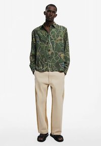 Overhemd in groen met bloemmotieven; gecombineerd met beige broek. Gladde stof met een losse pasvorm en zwarte sandalen.