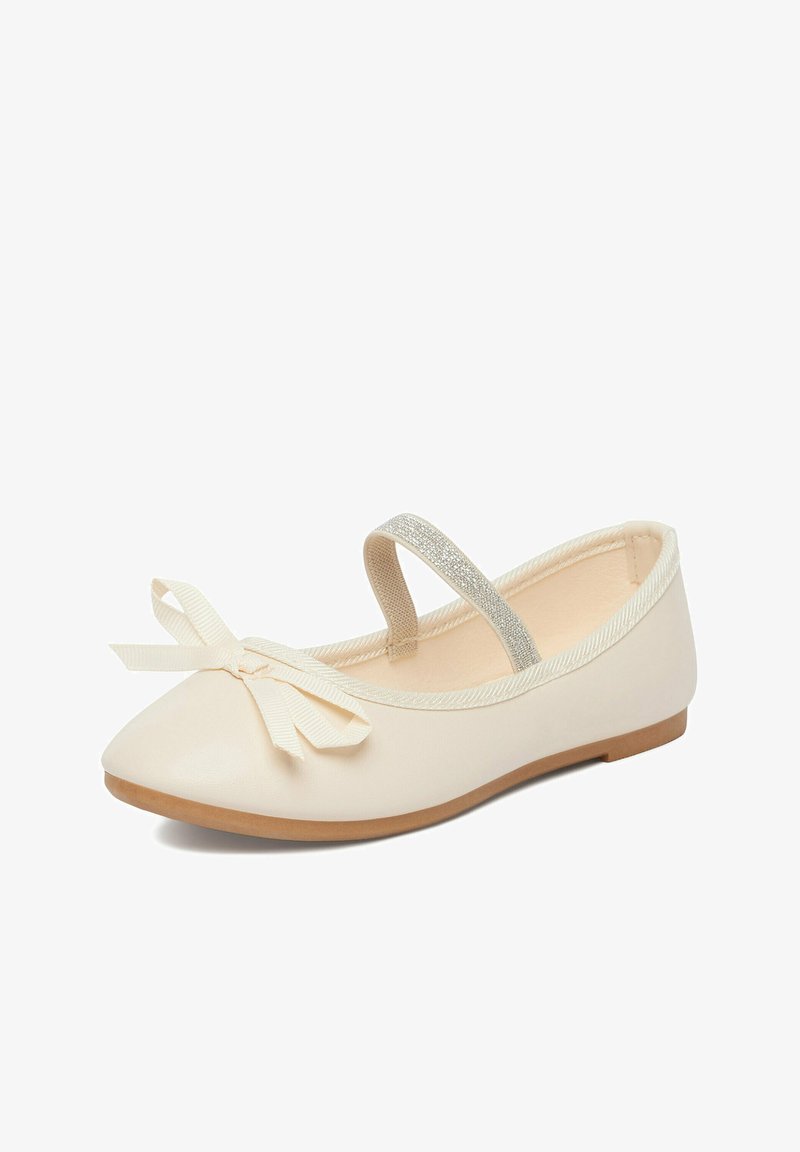 Scarpa bassa color crema con un piccolo fiocco sulla punta e un’elastica scintillante sopra, caratterizzata da una suola marrone chiaro.