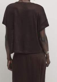 Maglietta corta a maniche corte di colore bordeaux con una vestibilità ampia, realizzata in un materiale testurizzato. Presenta un collo rotondo e un orlo leggermente accorciato.