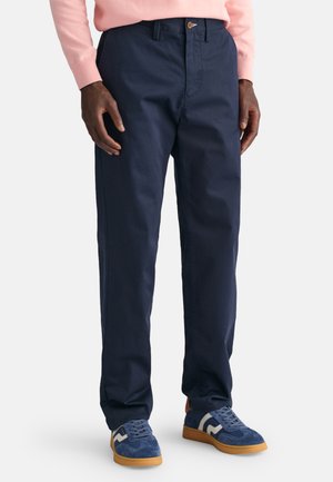 Navy blue chinos made of durable cotton, featuring a straight cut, button closure, and side pockets, paired with blue sneakers.